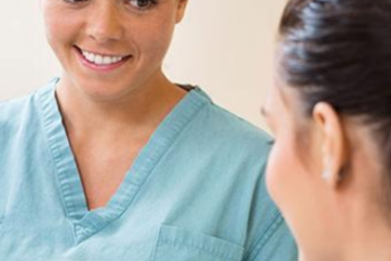 A woman in scrubs smiling to another woman